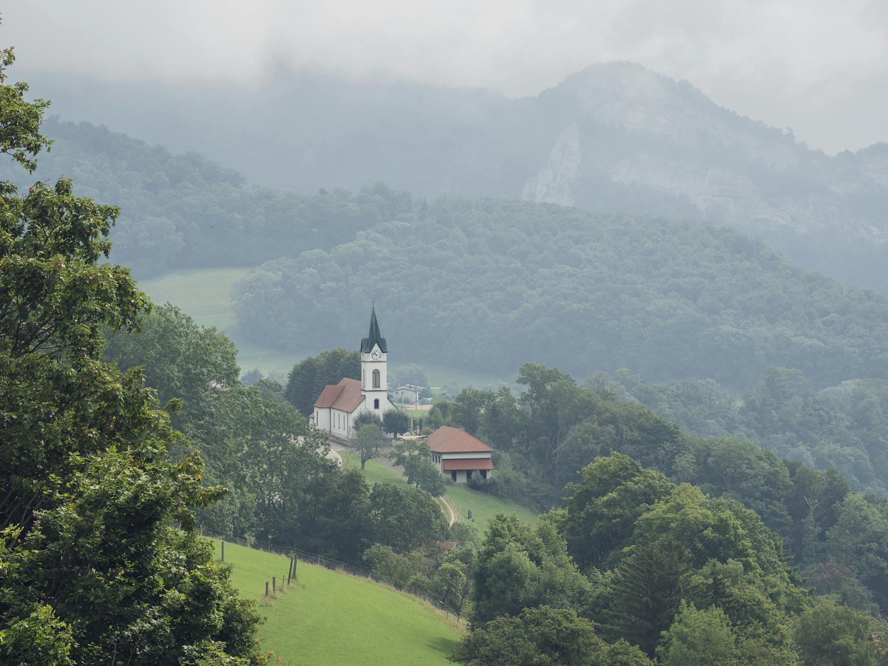 Picturesque valley scene with a church, forest, and misty mountains.